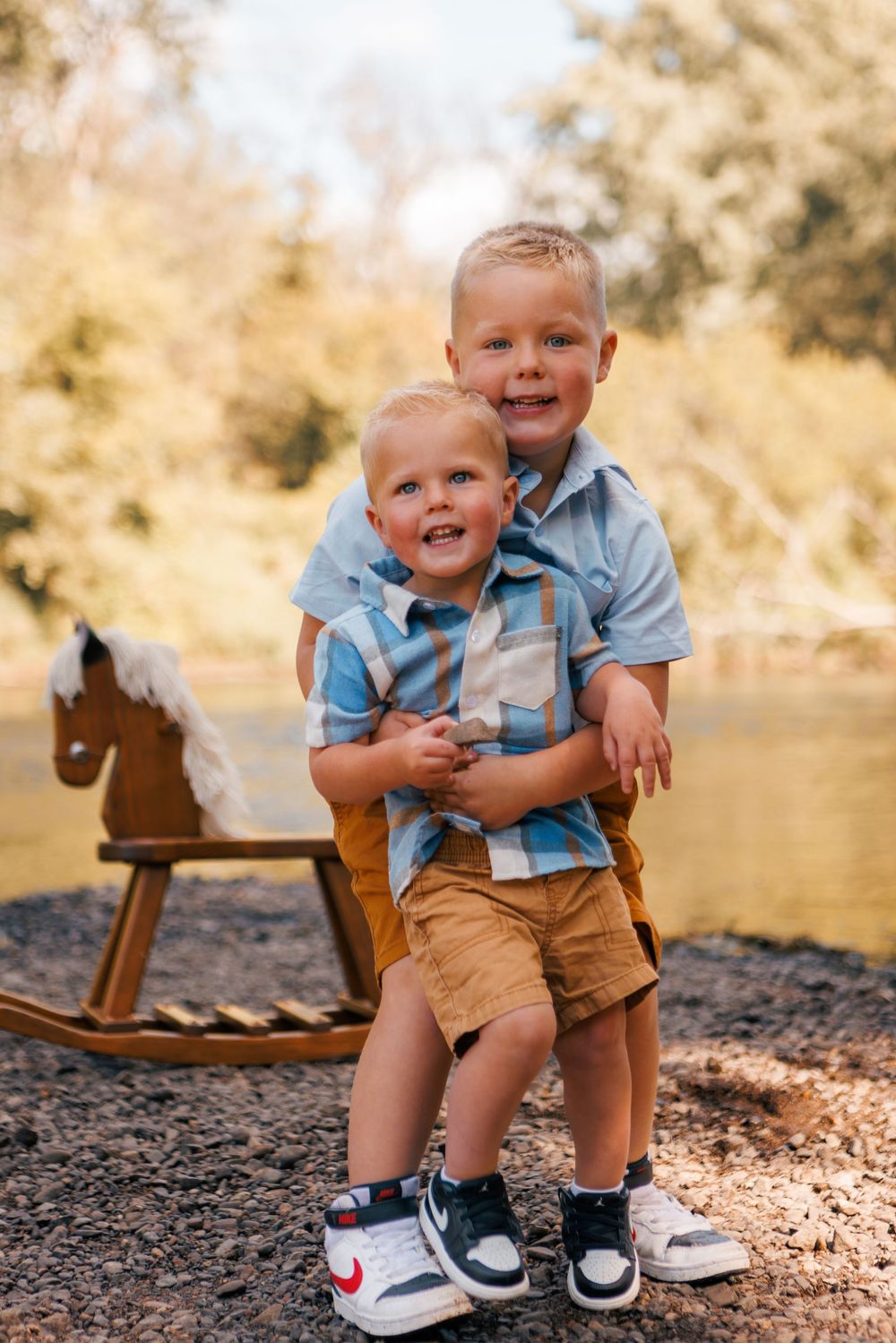A child in blue shirt and brown shorts sits outdoors on a rustic wooden rocking horse at golden hour.