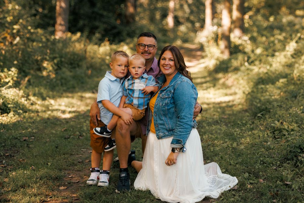 Group sitting together outdoors on a sunny autumn day in a wooded area during a family photography session.