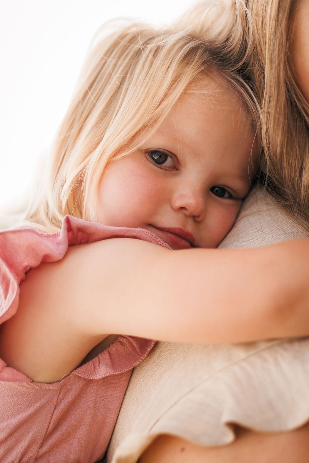 A young child in a pink shirt lying down on white bedding with a sleepy, dreamy expression.