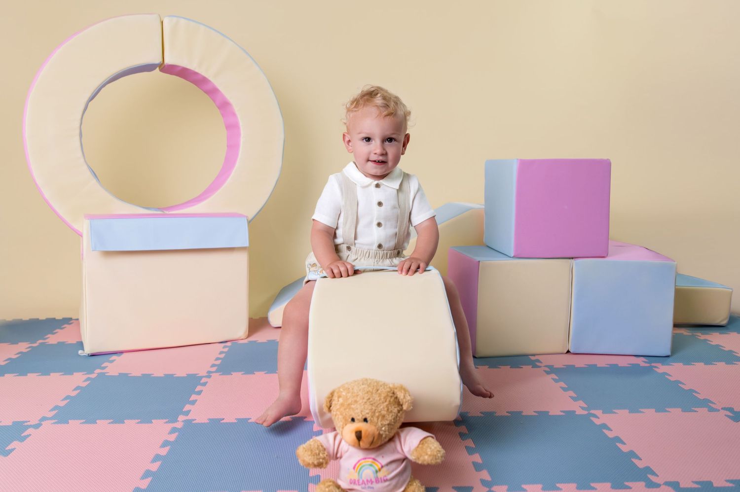 Baby boy celebrating first birthday with pastel letter blocks and bunting during soft play photoshoot in Suffolk.