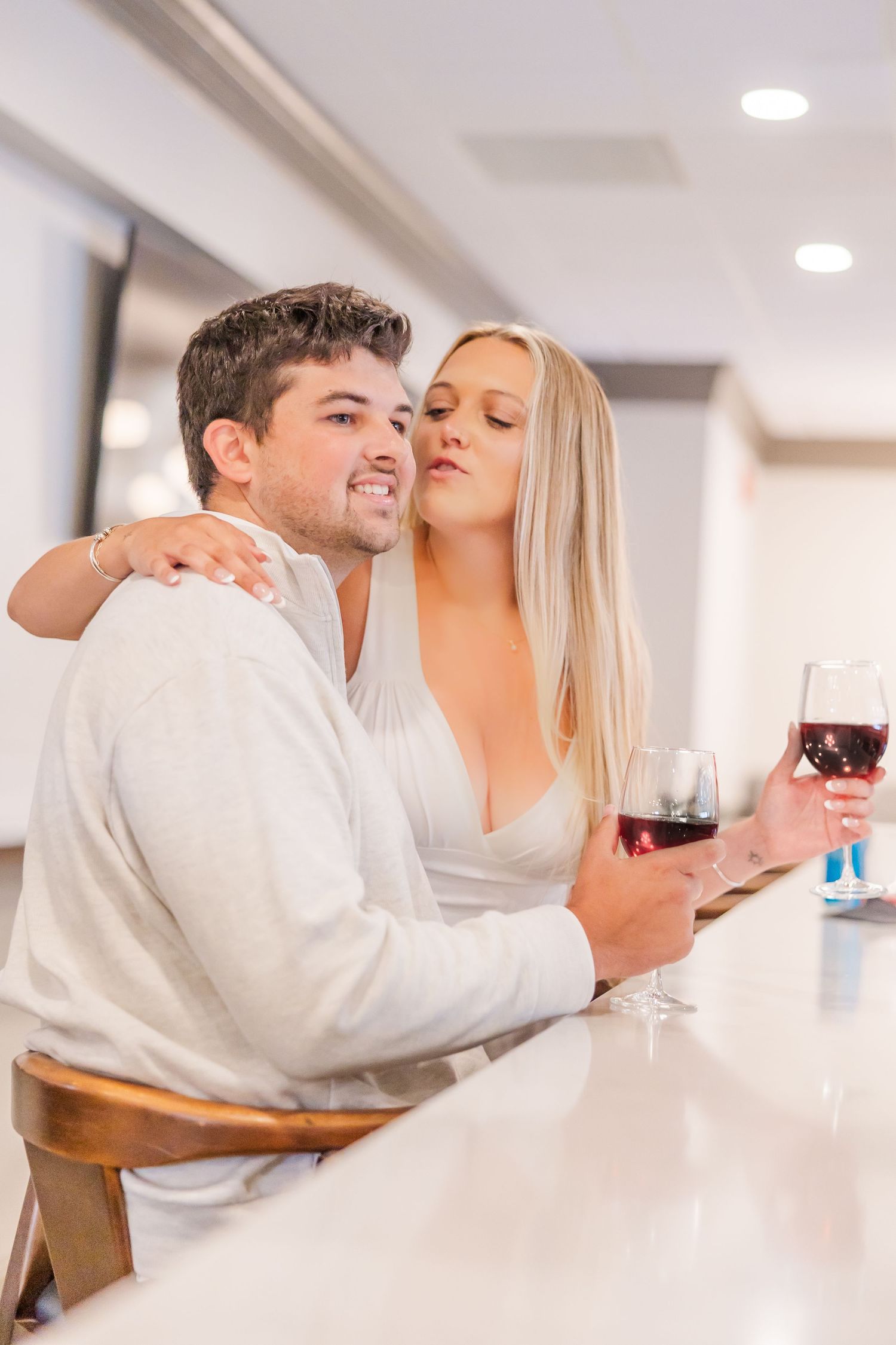 A couple enjoys red wine together at a white bar counter in an intimate moment.
