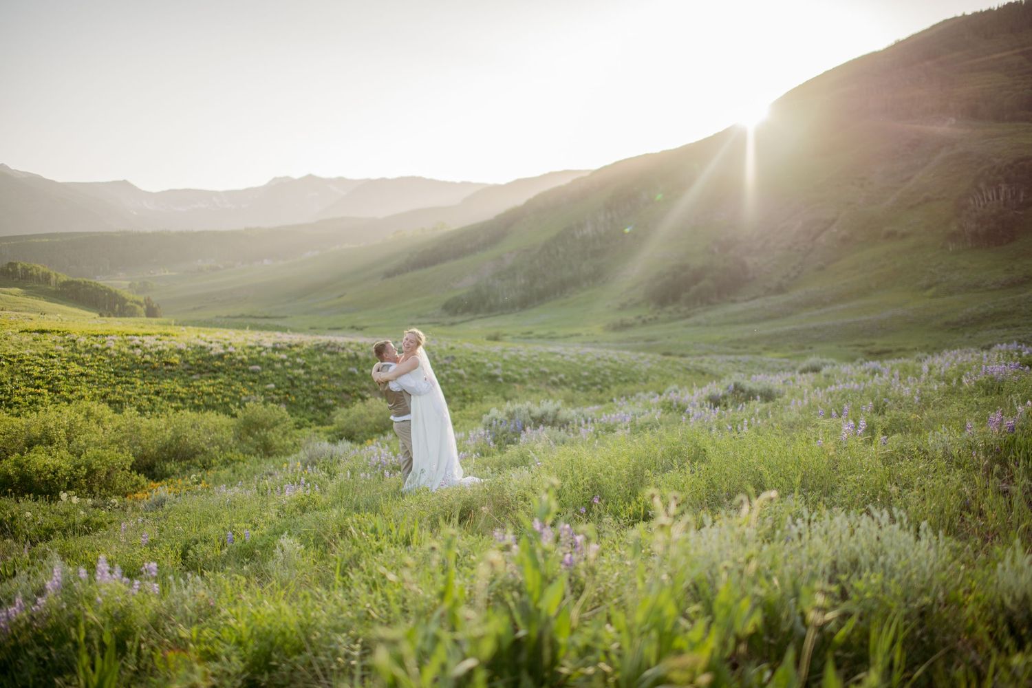 A romantic wedding couple stands back-to-back in a golden field during sunset.
