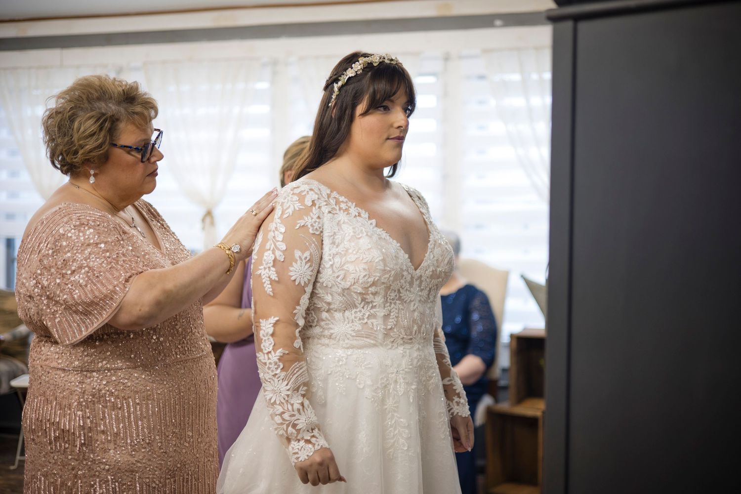 A bride gets help getting dressed for her wedding day with cream colored details and delicate lace trim details.