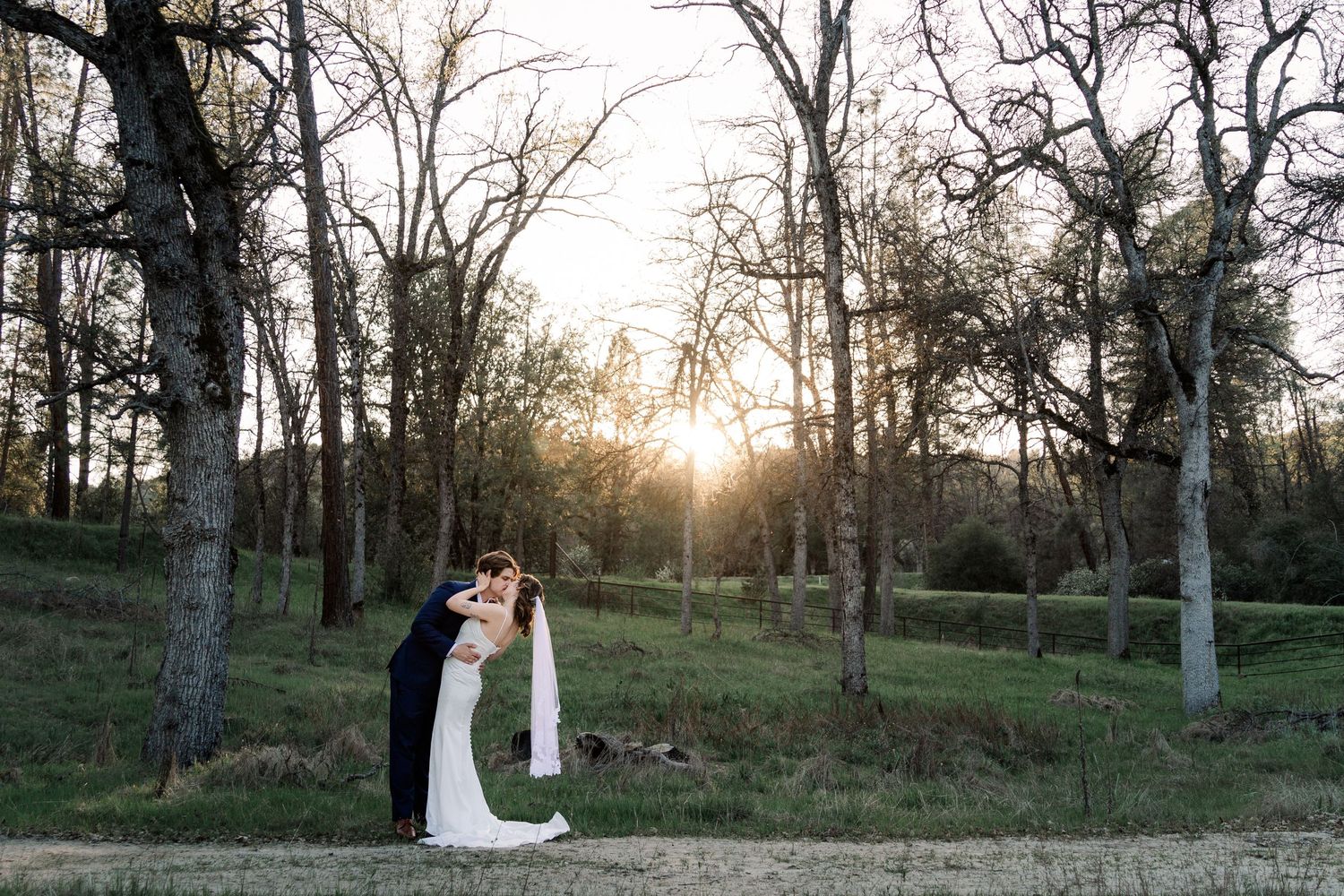 A couple shares an intimate moment at sunset in a wooded area during their wedding.