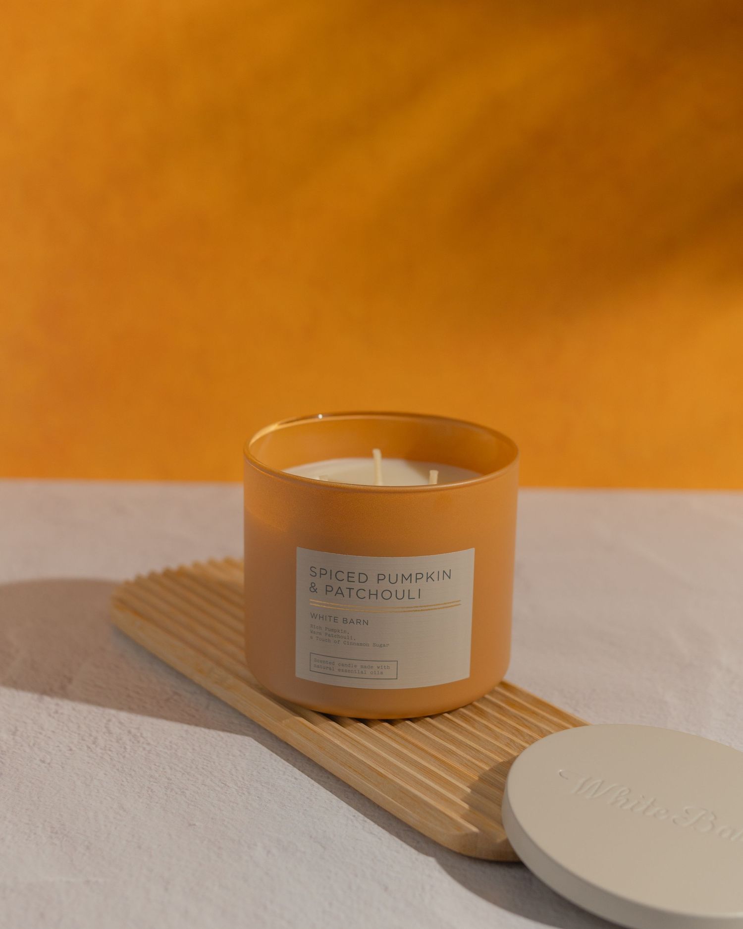 Spice pumpkin candle sitting on wood board with a orange background