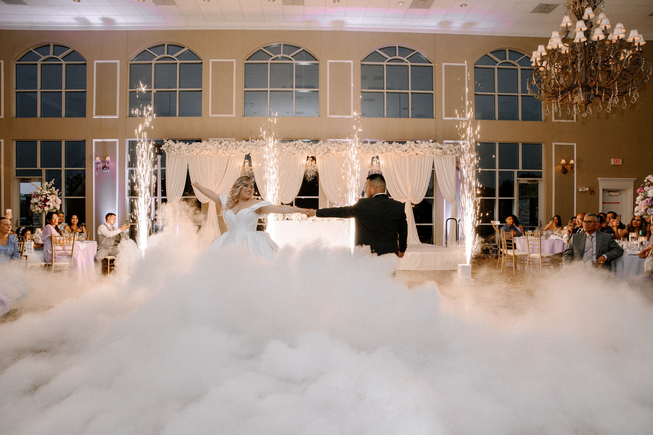 A beautifully decorated wedding reception ballroom with chandeliers and white drapery creating an elegant atmosphere.