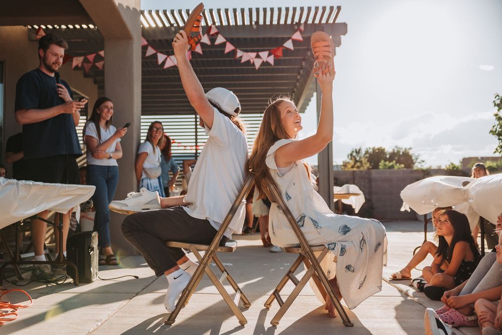 Wedding guests enjoying festivities under a pergola at an outdoor reception with white umbrellas and string lights.