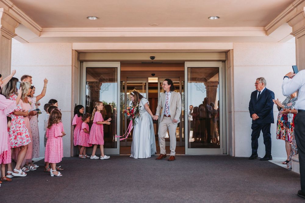 Wedding party exits building while guests line up on both sides holding flower petals for celebratory send-off.