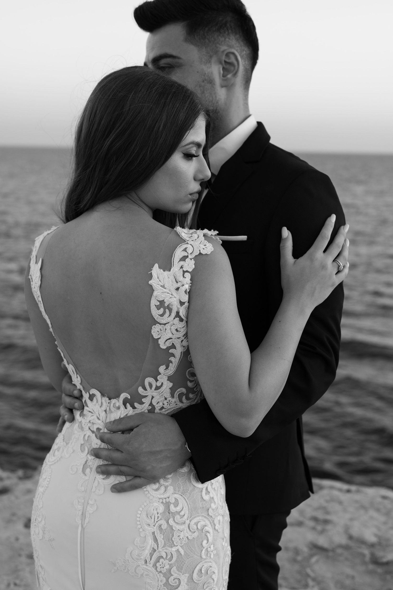 A bride and groom standing under white arches with a beautiful blue ocean view in the background.