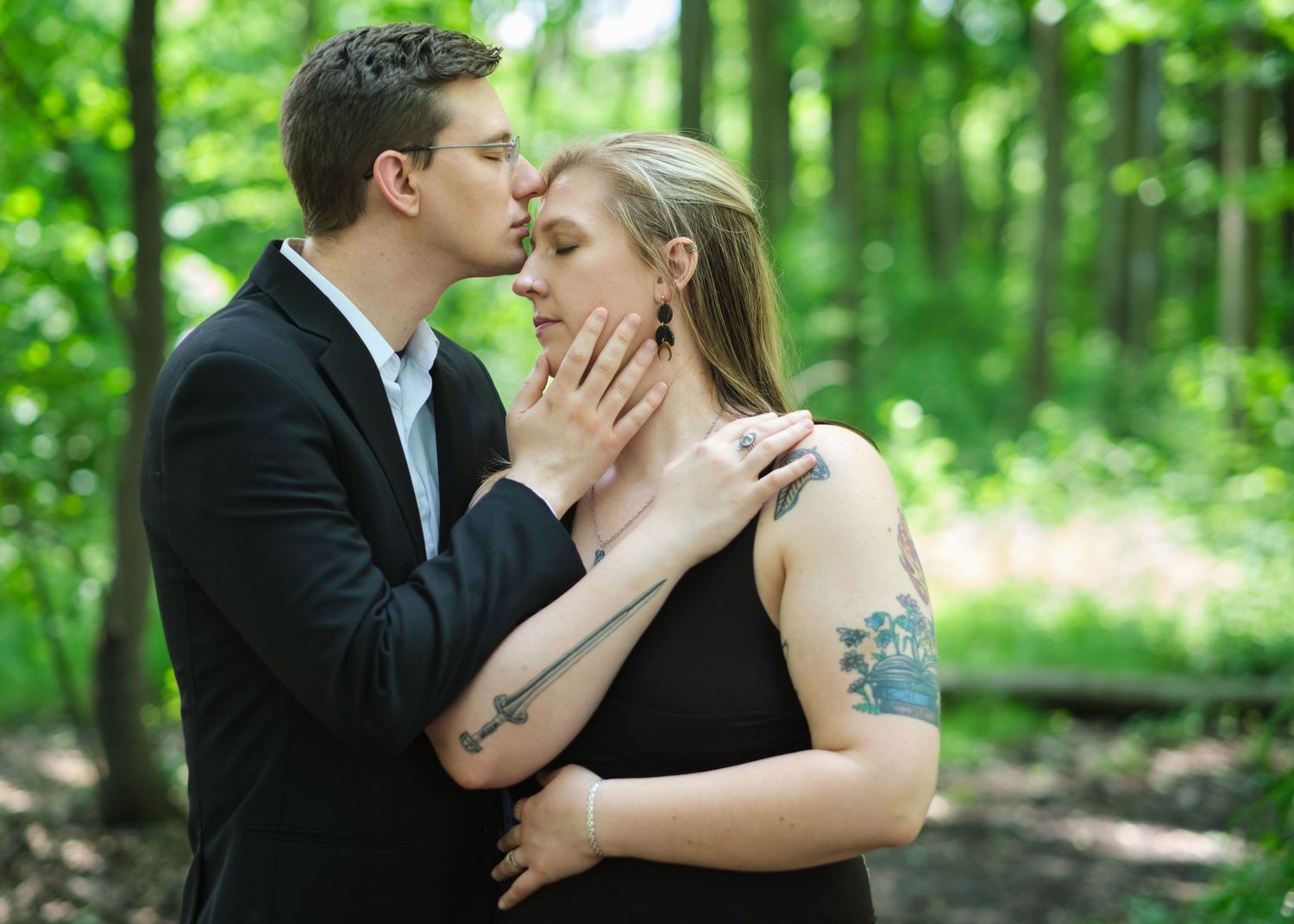 Portrait of a couple in the forest with the husband gently kissing his wife's forehead.
