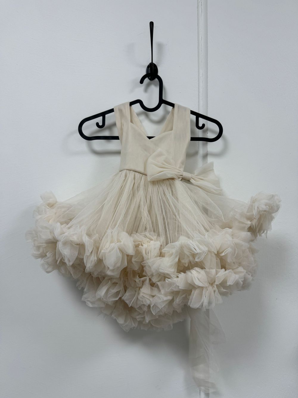Elegant cream-colored tutu skirt with fluffy layers of tulle displayed on a black hanger against a white wall.