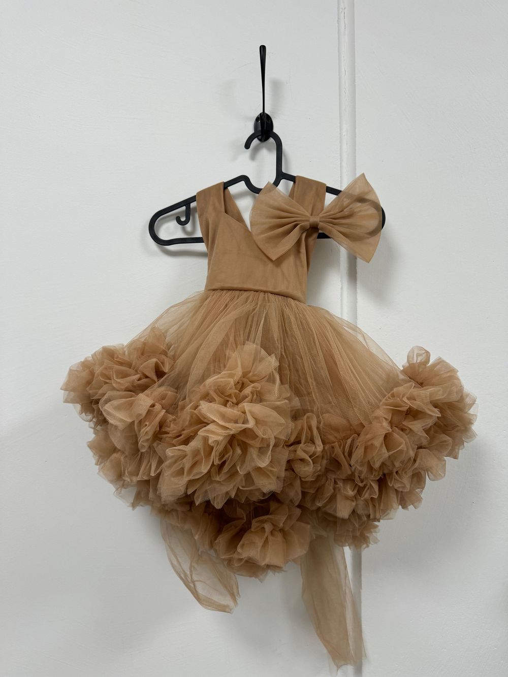 A fluffy champagne-colored tulle layered tutu skirt hanging on a clothing hanger against a white wall.