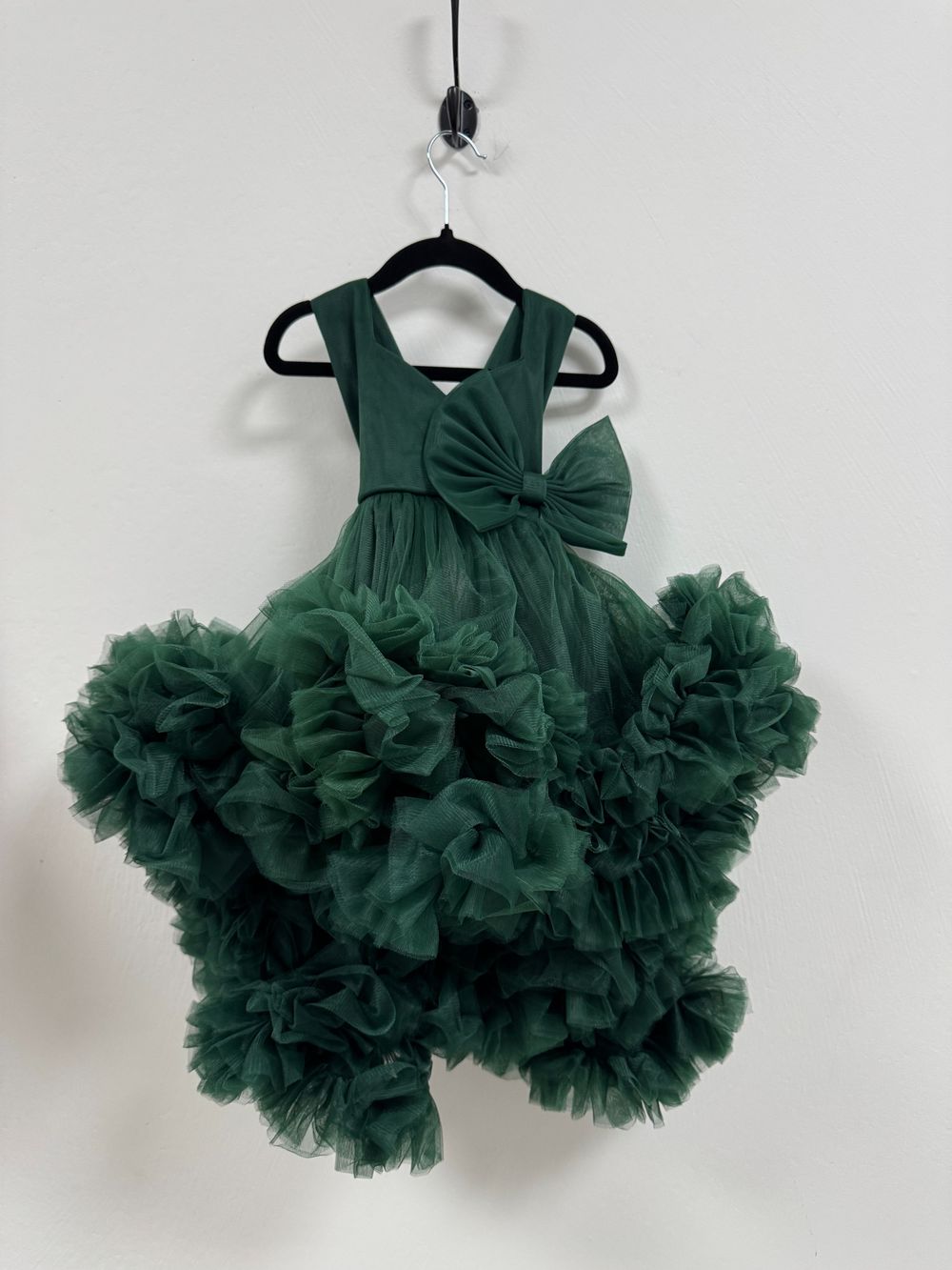 A luxurious emerald green tulle dress with ruffled layers and a large bow detail hangs on display.