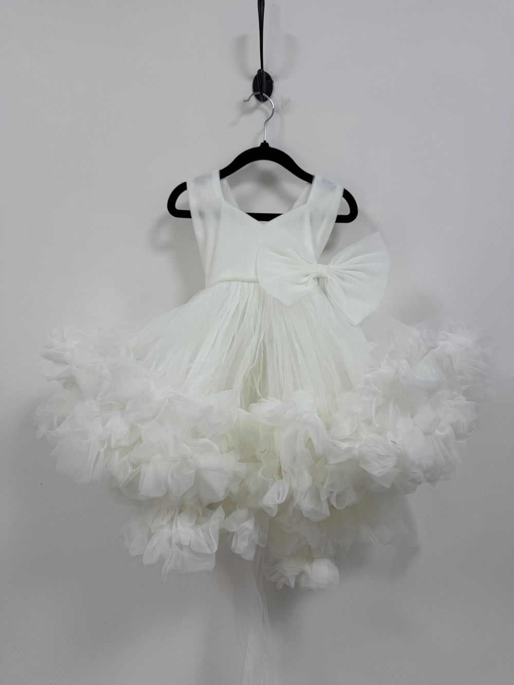 Fluffy white tulle tutu skirt with ruffled layers and bow accent displayed on black hangers against grey background.