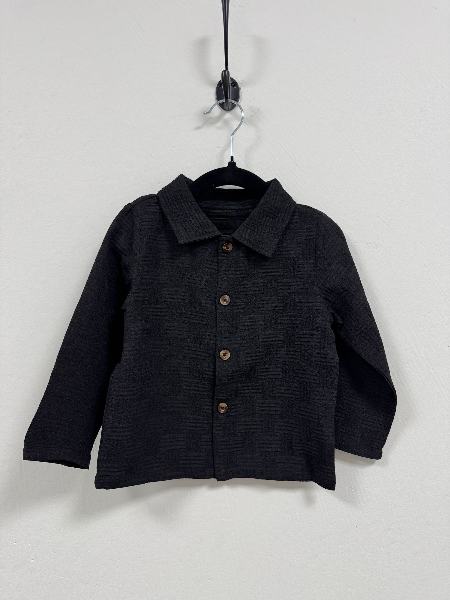 Black textured button-up jacket with collared neckline hanging on display against white background.