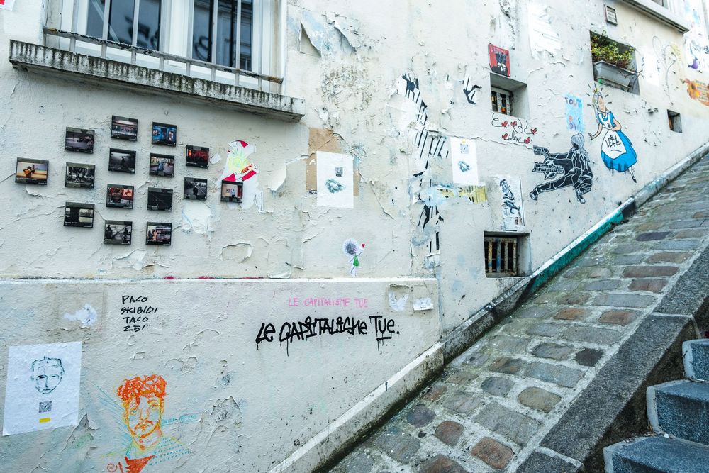 Street art and posters decorate a concrete wall along stone steps in an urban environment.