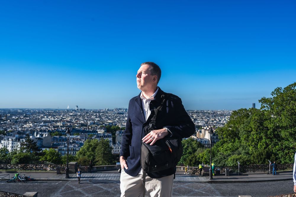 Tourist enjoys scenic overlook of Paris cityscape against bright blue sky on sunny day.