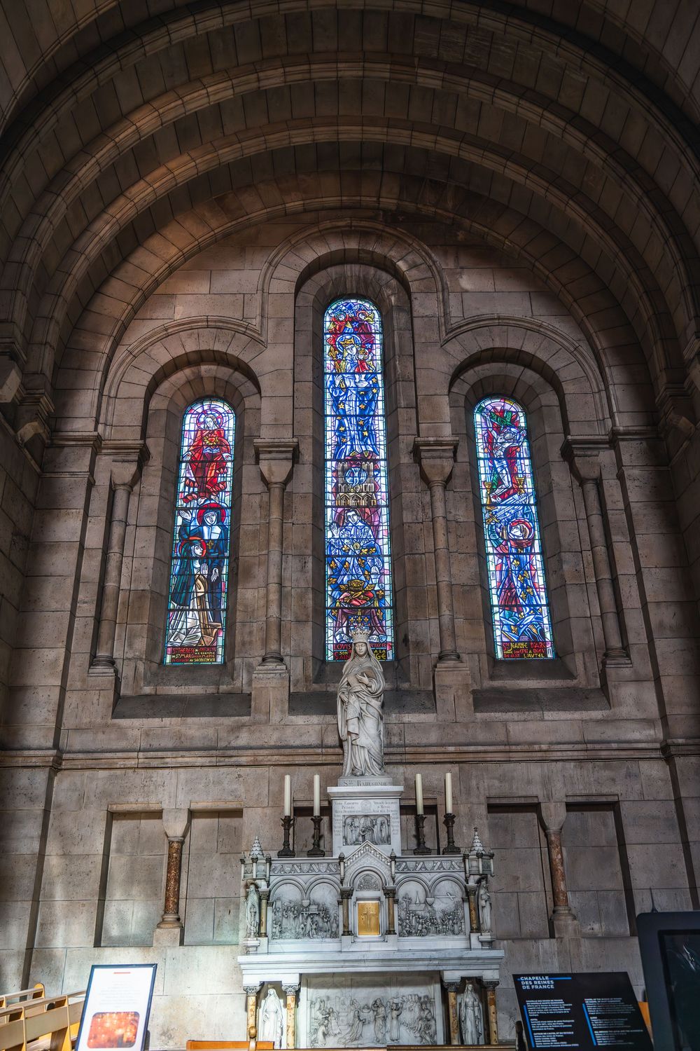 Gothic church interior featuring arched stone walls and colorful stained glass windows with intricate religious designs.