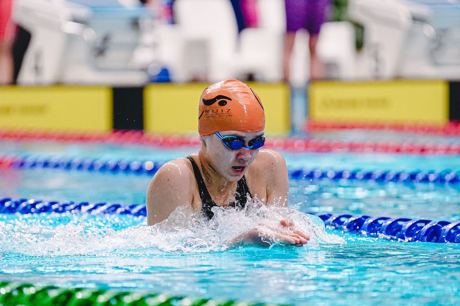 A swimmer performs freestyle stroke in a bright blue swimming pool while wearing swim goggles.