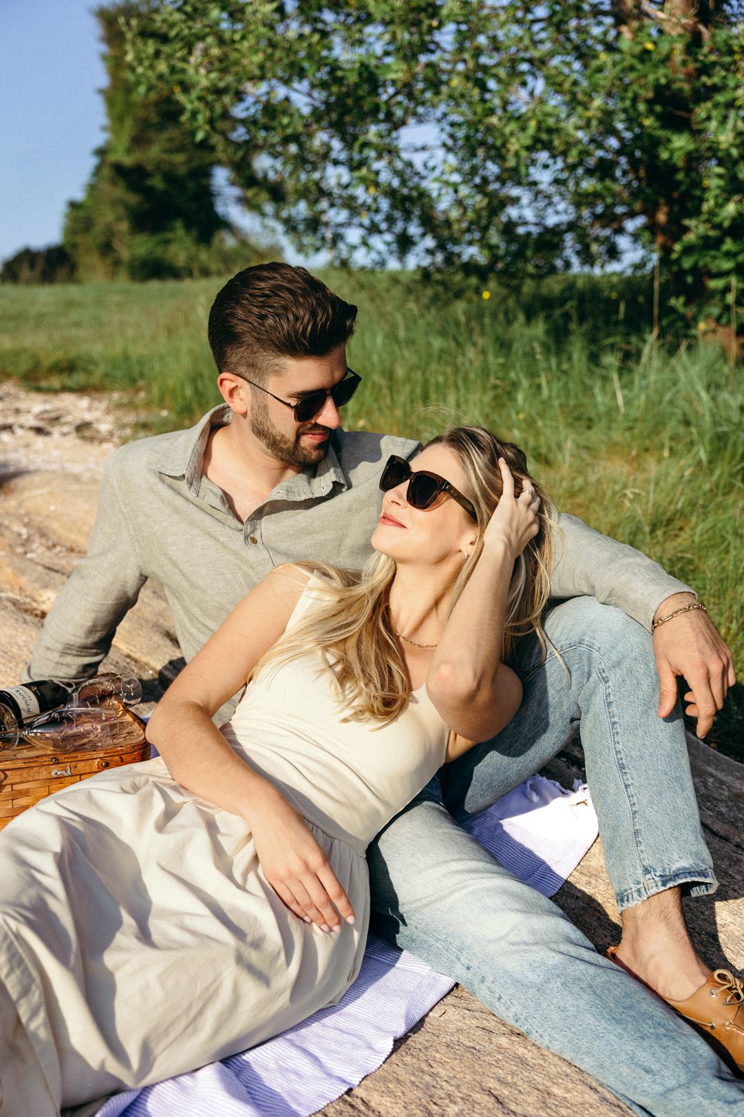 Romantic couple relaxing on blanket outdoors wearing sunglasses in summer sunshine.