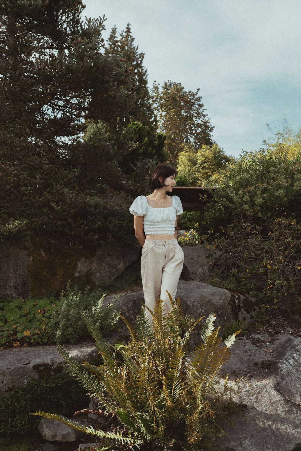 A vintage-inspired outdoor scene with a light blue crop top and high-waisted pants outfit atop a large rock formation.