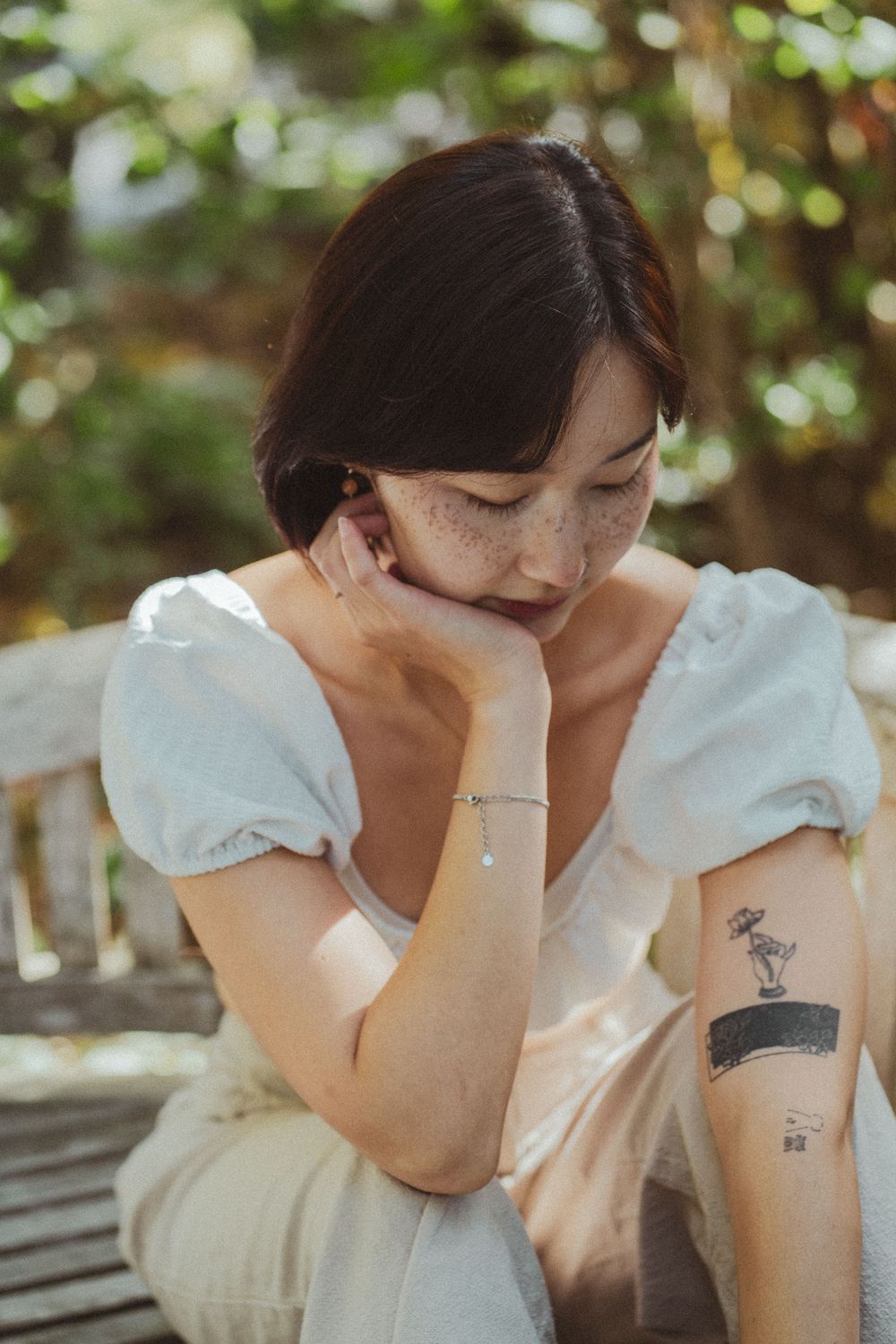 Someone in a white blouse sitting outdoors displays emotional distress while covering their face.