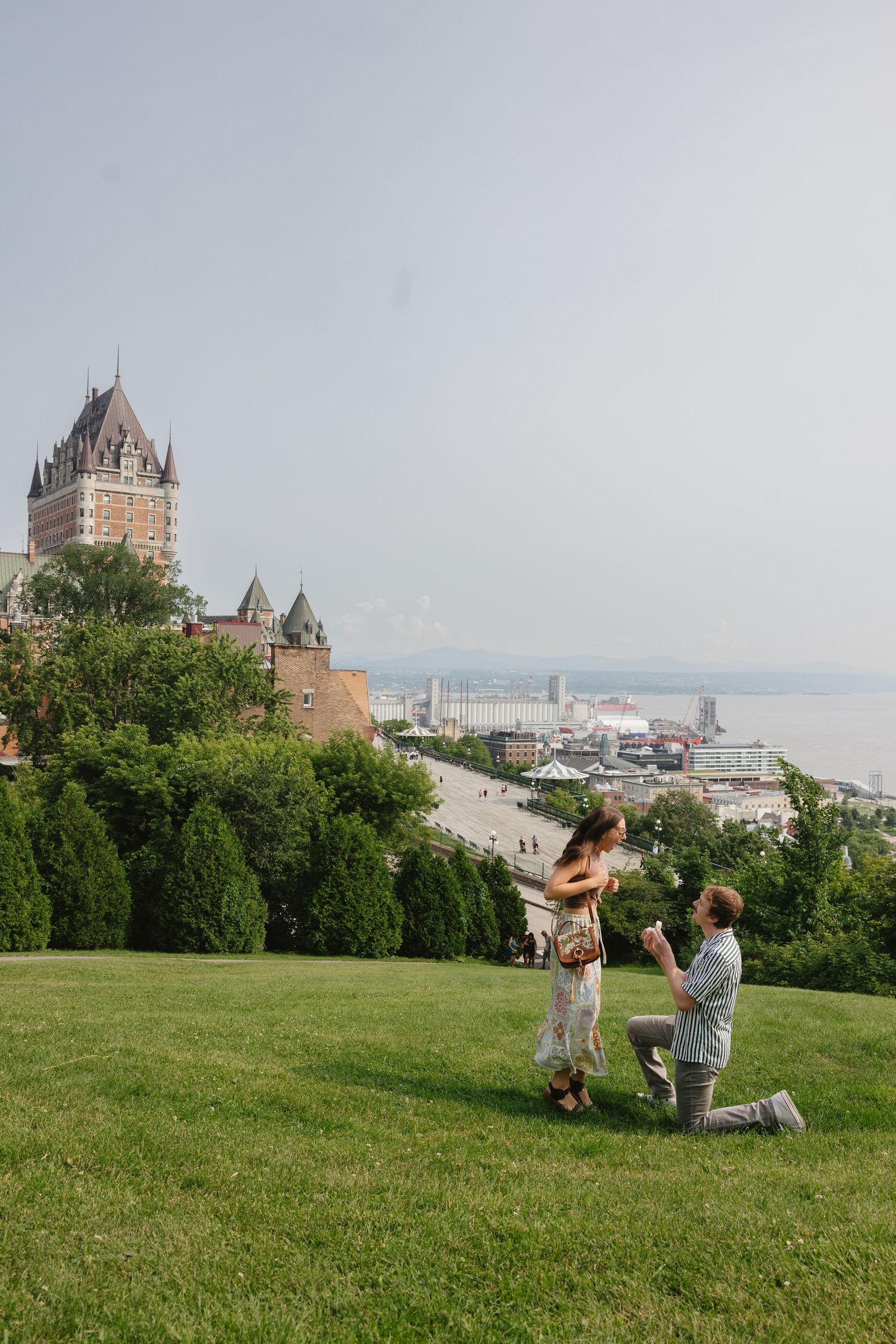 A romantic proposal takes place on a grassy hill overlooking Quebec City with Chateau Frontenac in the background.