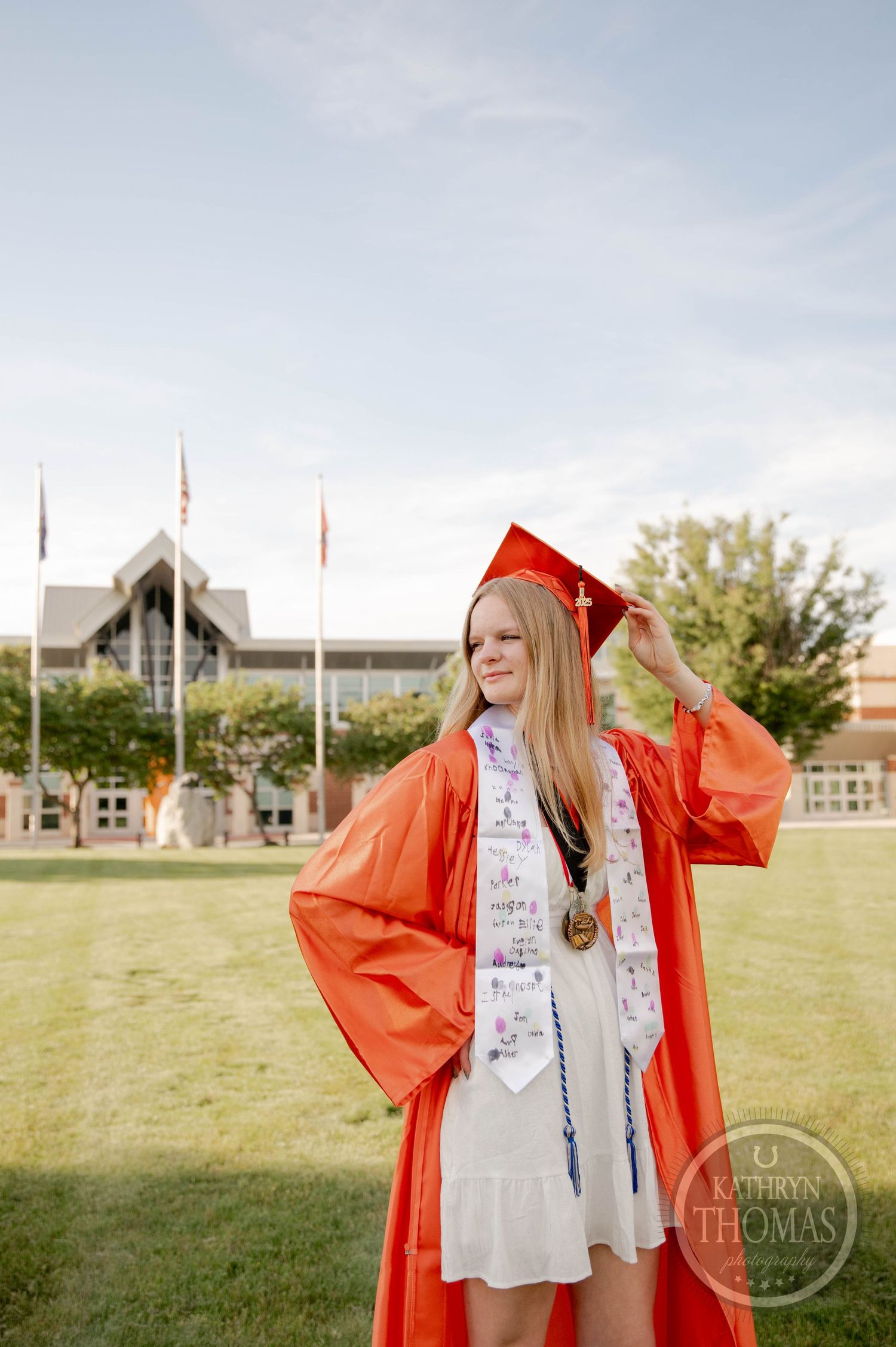 Graduate in bright red cap and gown celebrates outdoors on graduation day with medal and decorative stole.