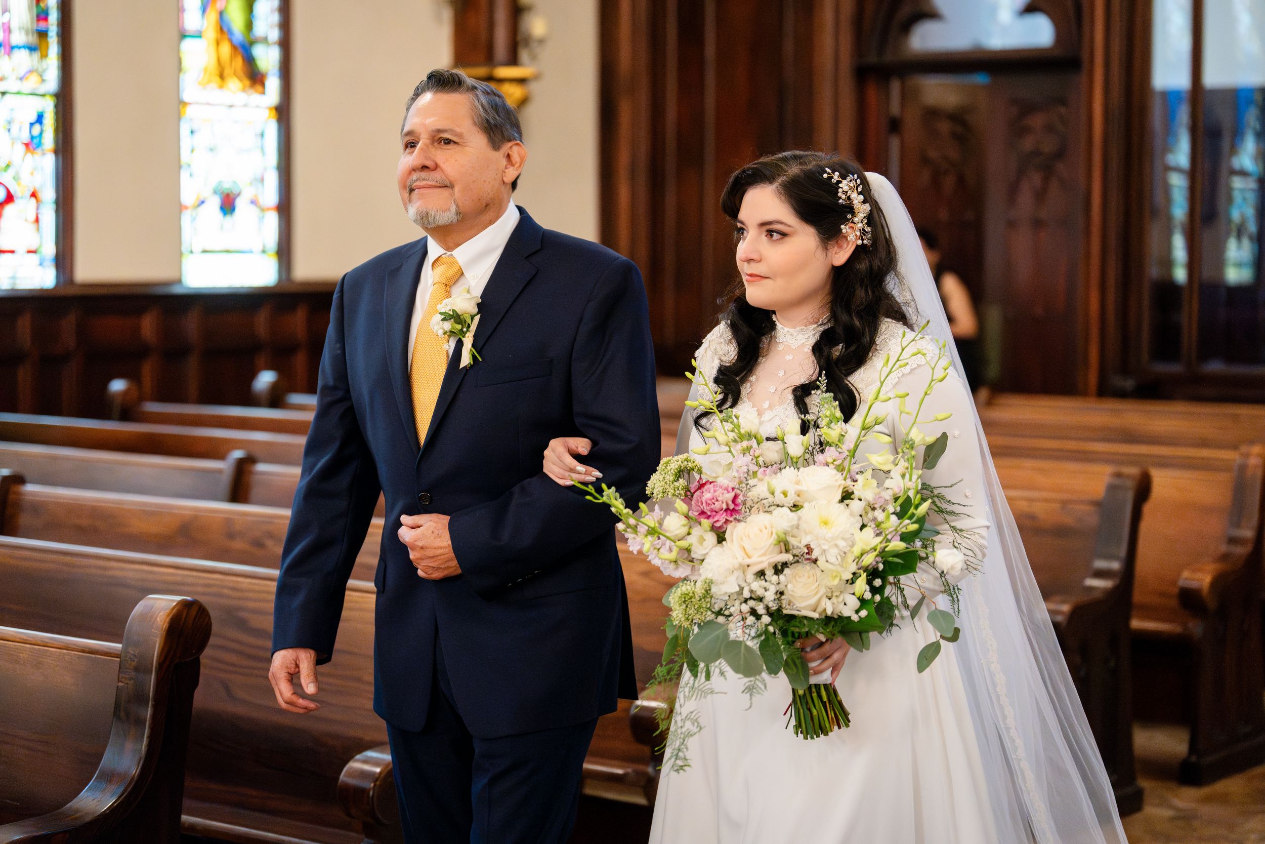 Wedding couple walks down the aisle of a beautiful wooden church interior with floral bouquets and decorations.