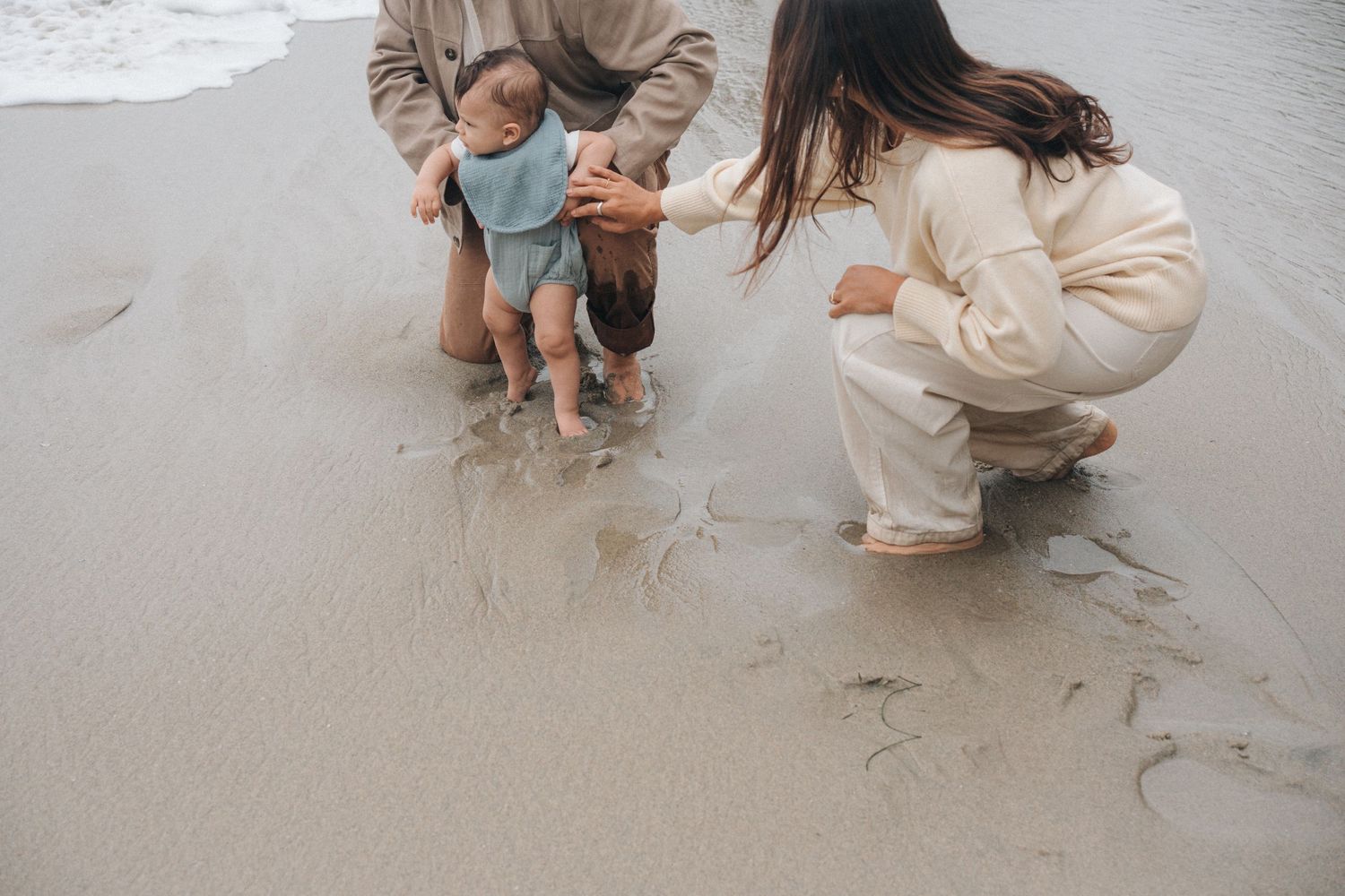 People in beige and blue outfits crouching on a sandy beach while playing together.