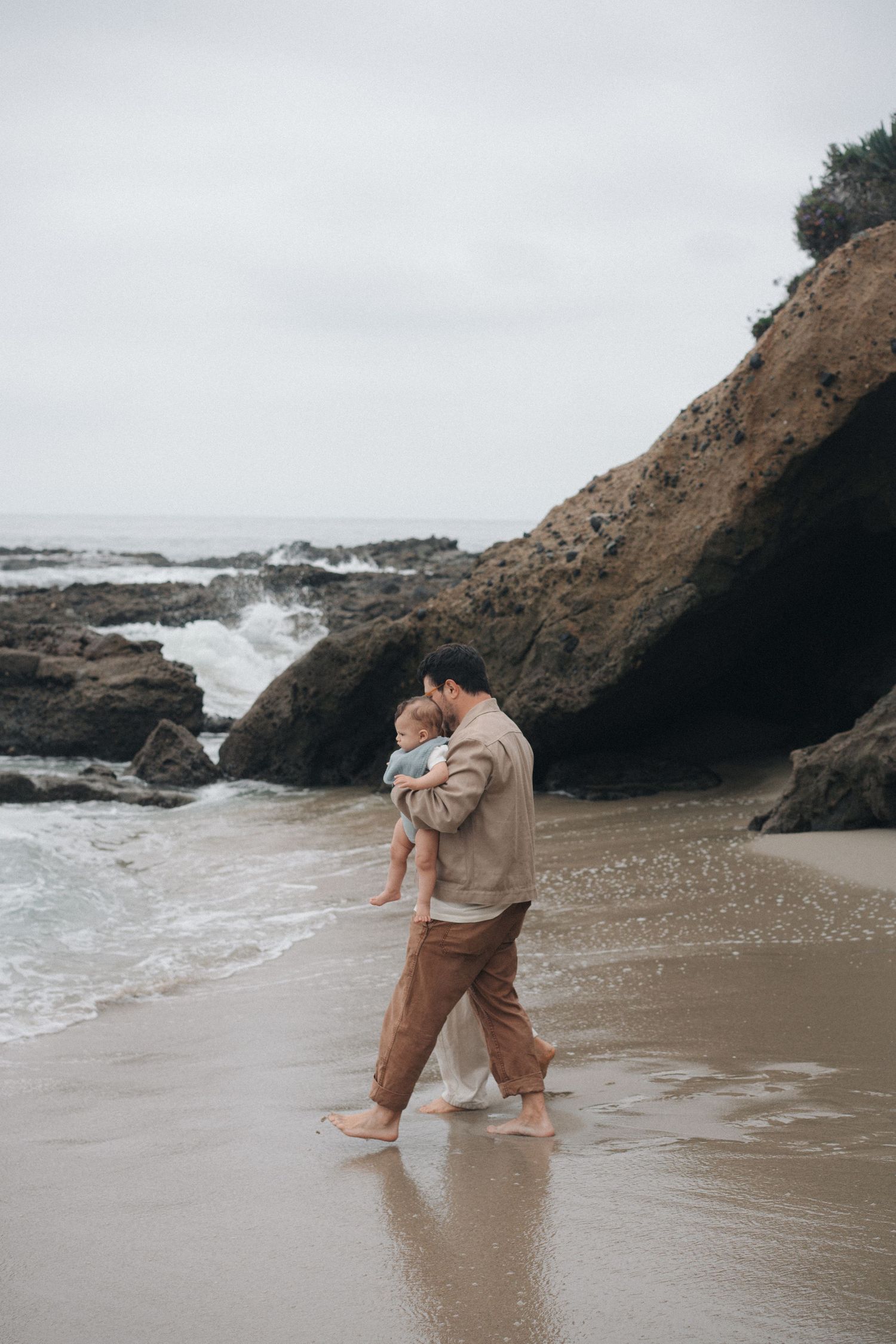 Romantic couple dancing and embracing on a misty beach with rocky cliffs and crashing waves in the background.