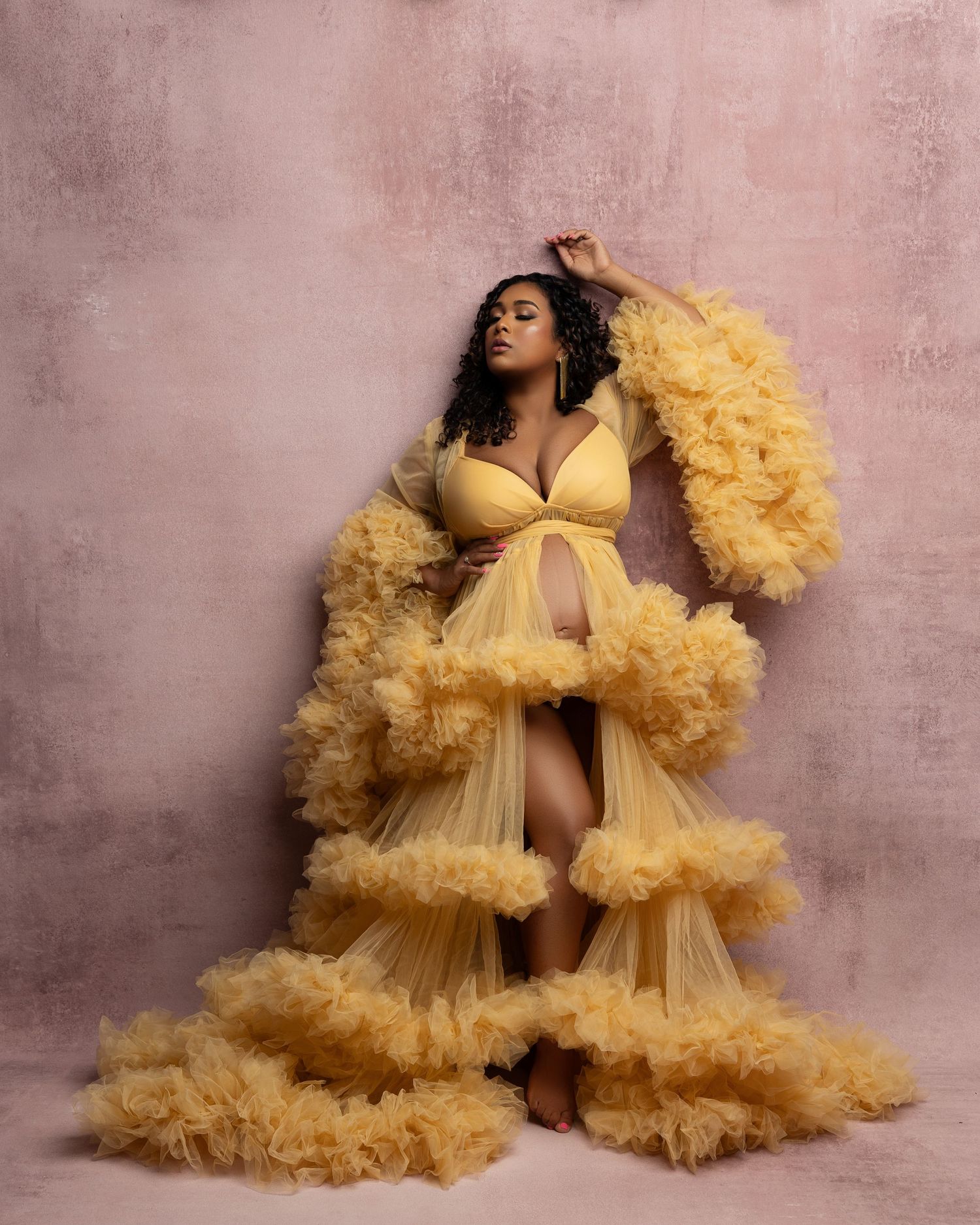 Pregnant woman in flowing mauve gown poses elegantly against white background during maternity photoshoot.
