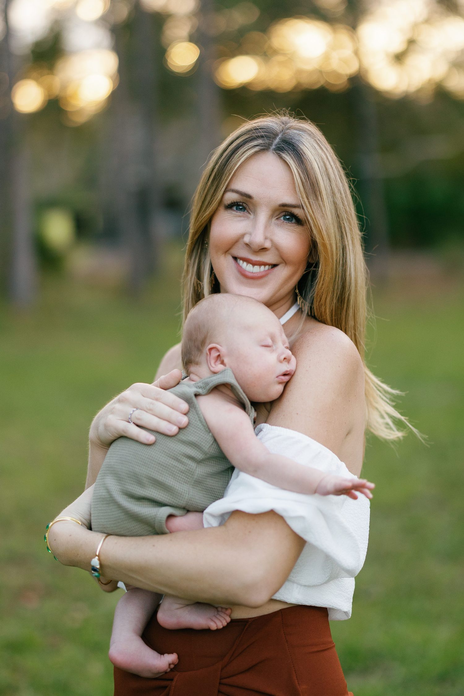 A tender moment with a mother holding a sleeping baby outdoors with a soft bokeh background.