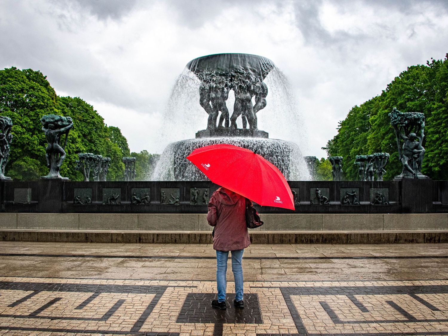 Misty panoramic view of a park monument with red umbrella silhouette against cloudy sky.