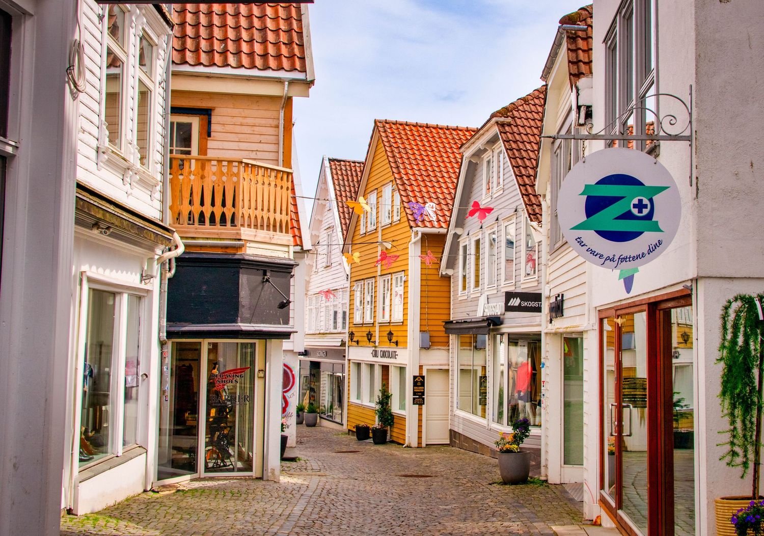 Narrow cobblestone alley between traditional white wooden buildings with orange tile roofs.