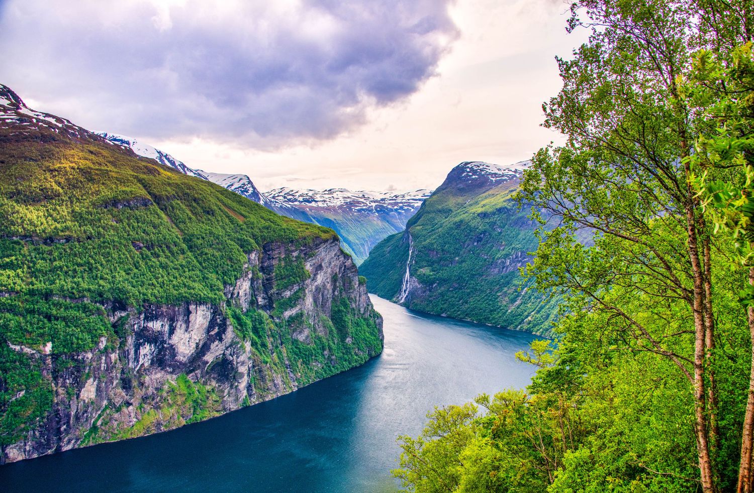 Dramatic fjord landscape with steep cliffs and calm waters under cloudy skies in Norway.