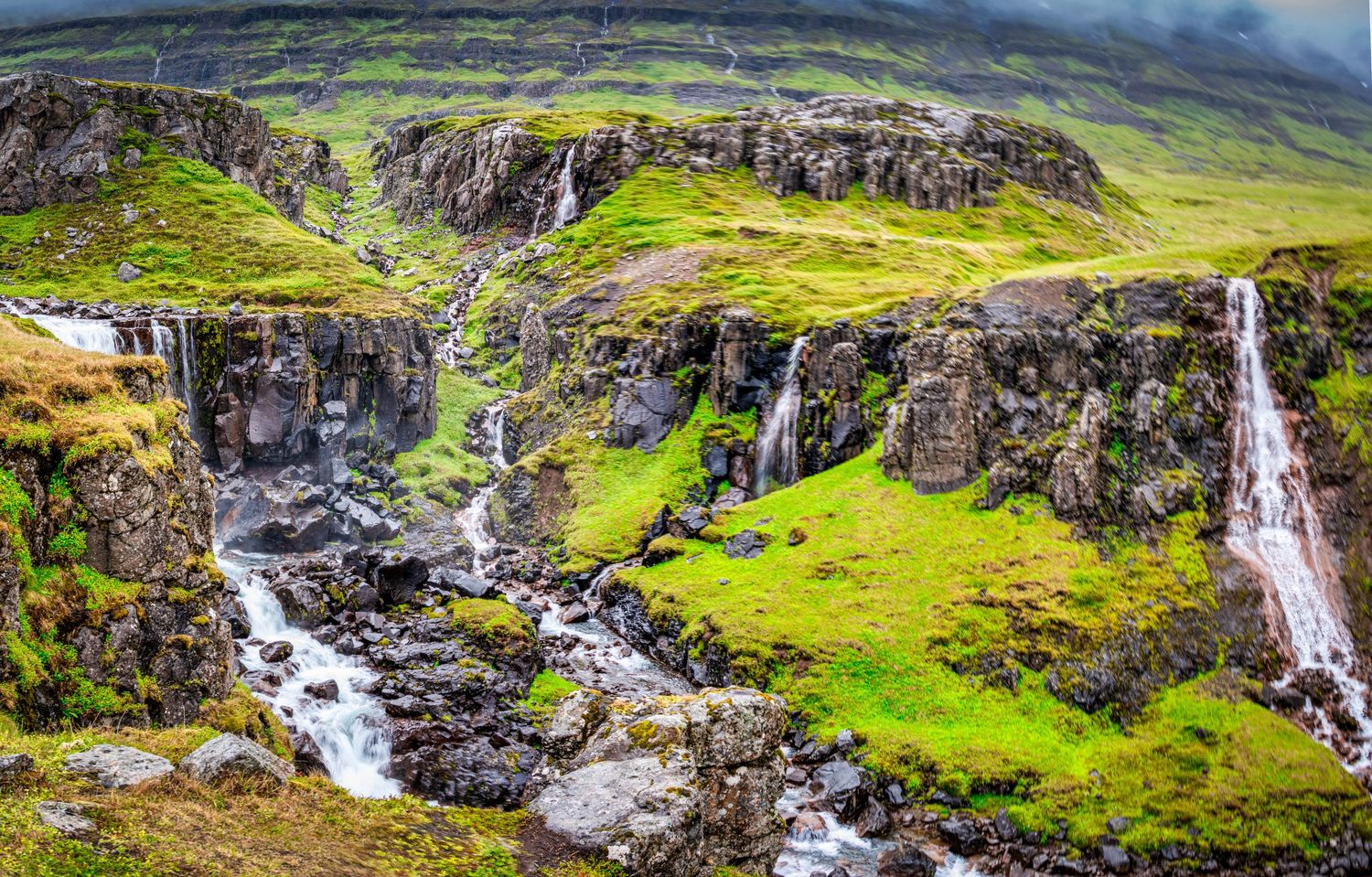 Multiple waterfalls flowing down green mountainsides in the rugged Faroese landscape.