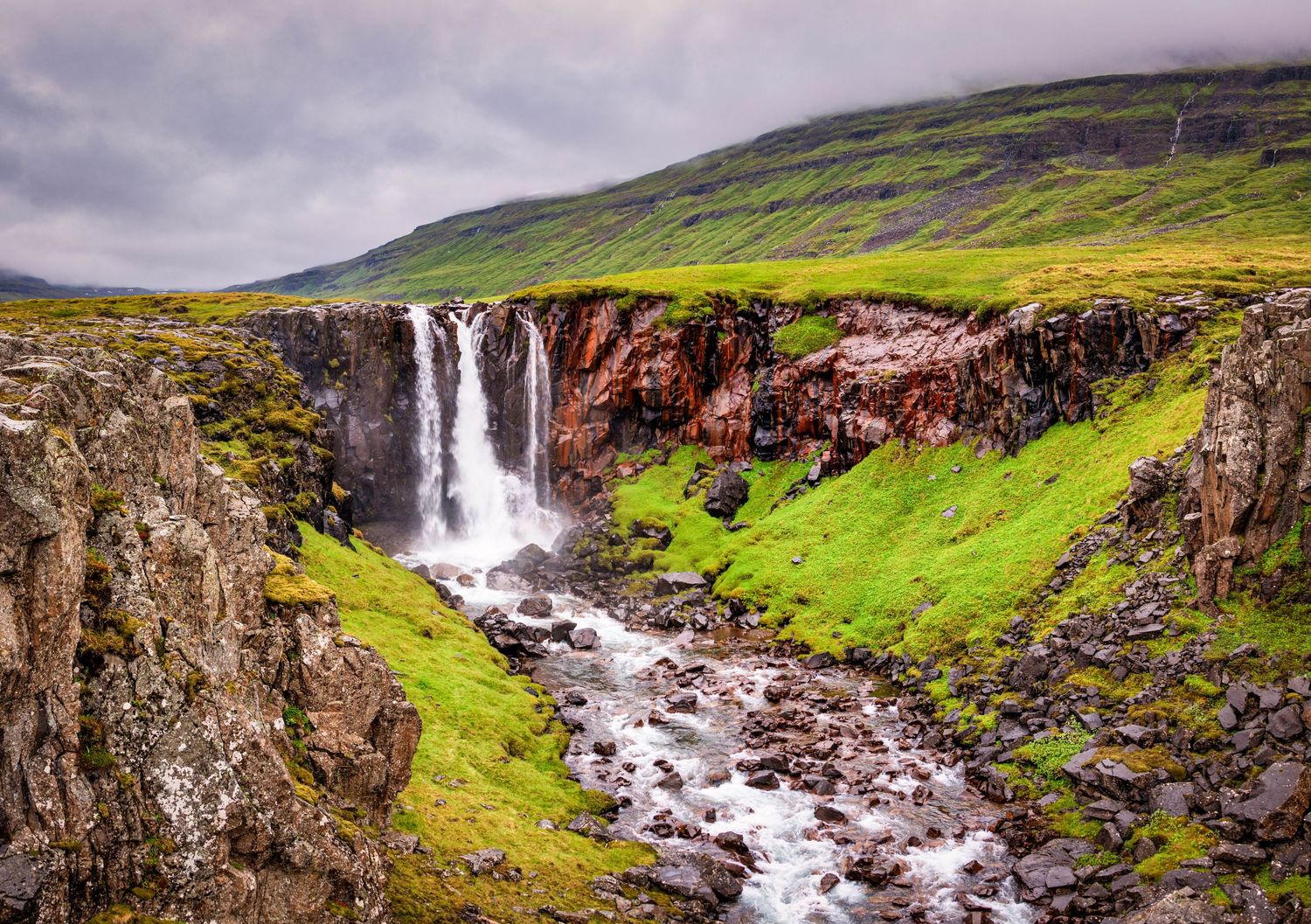Dramatic waterfalls cascade down rocky cliffs in the misty Faroe Islands landscape.