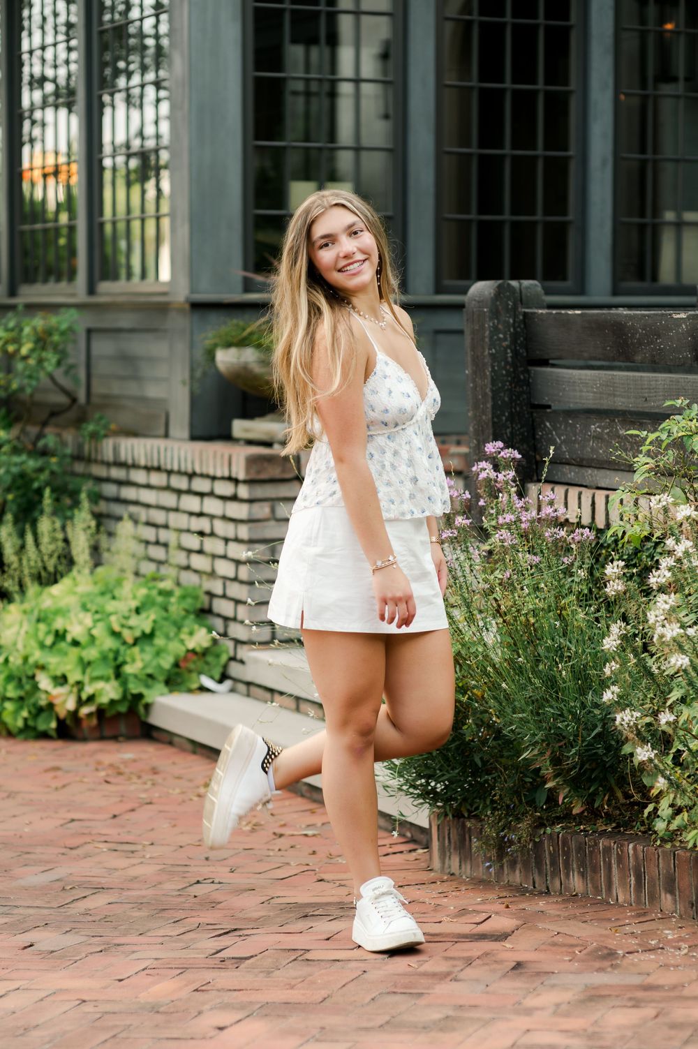 A casual summer outfit with white sneakers on a brick patio near garden flowers and windows.
