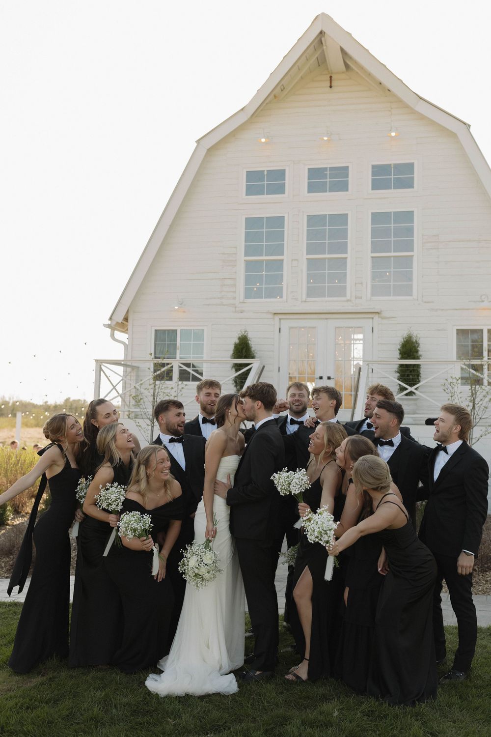 Wedding party poses for group photos in front of a white chapel with baby's breath bouquets.