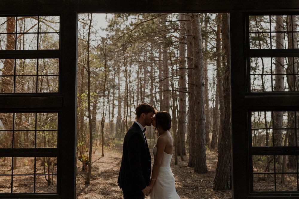 Silhouettes of a wedding couple framed by a wooden chapel structure in a forest setting.
