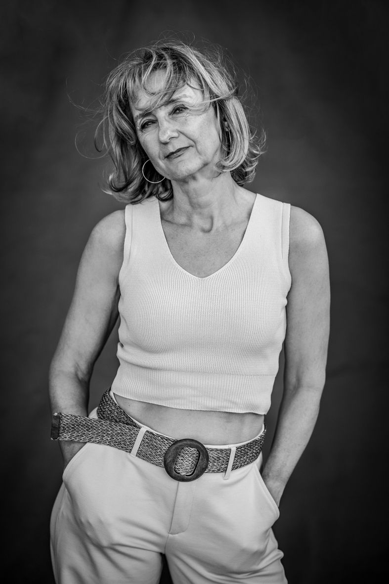 Schwarz-Weiß-Porträt einer Frau im hellen Top und heller Jeans, dreiviertel stehend mit wehendem Haar und sanftem Lächeln