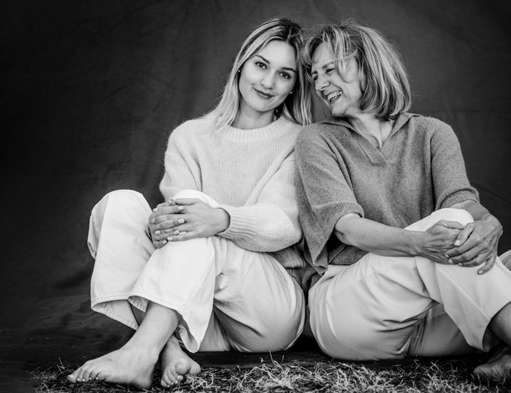 Herzlicher Moment zwischen Mutter und Tochter: Die Mutter lehnt sich lachend an, während die Tochter in die Kamera schaut.