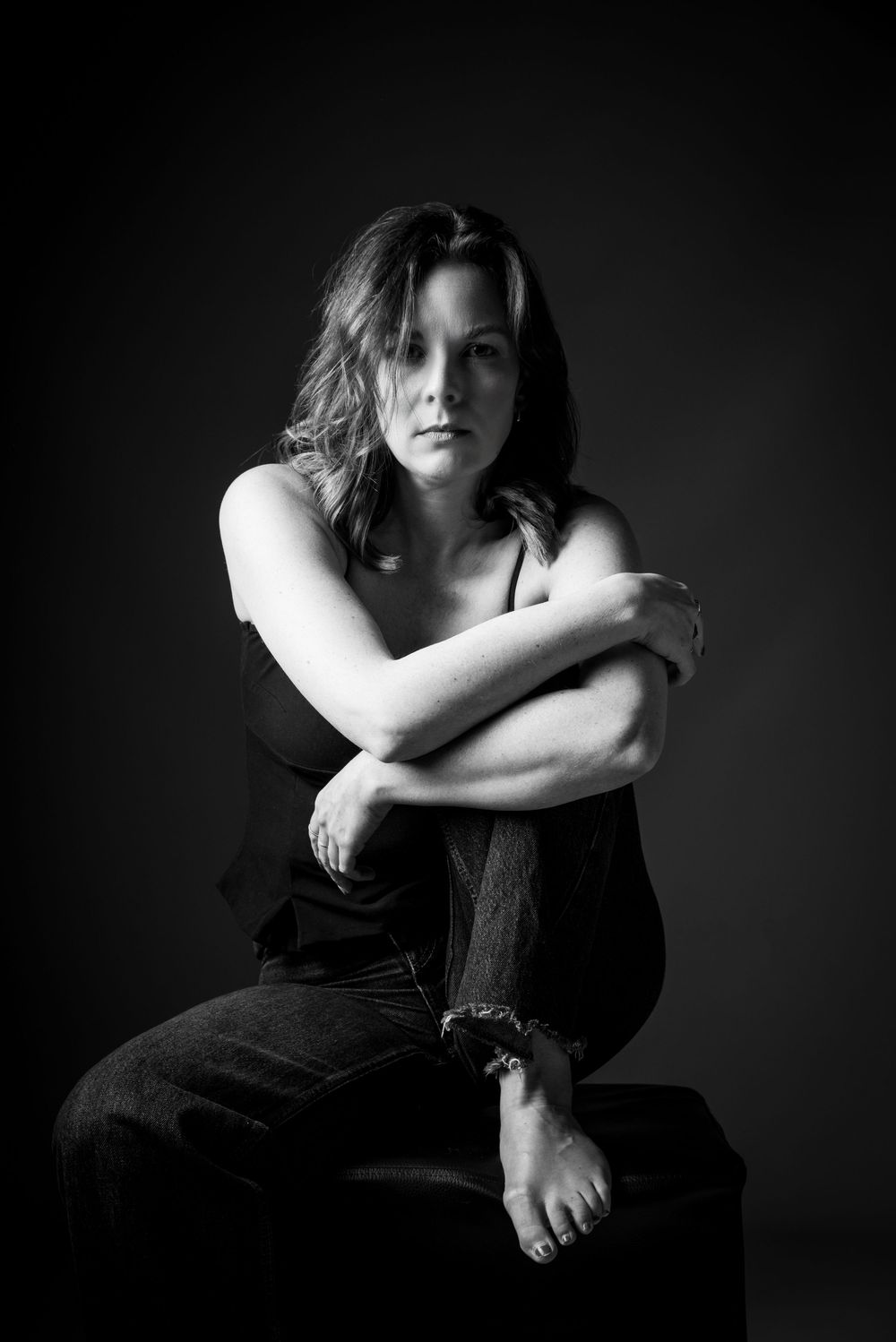 Frau sitzt auf Hocker, hat ihr Bein umschlungen  – stilvolles Schwarz-Weiß-Portrait im Fotostudio Gelsenkirchen-Hassel