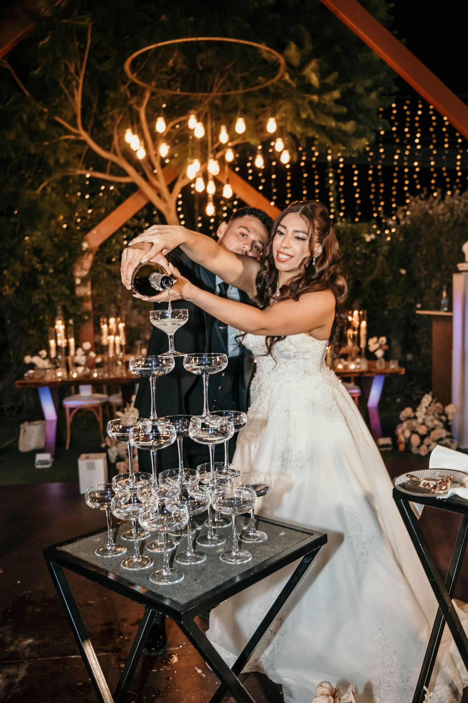 An elegant outdoor wedding reception setup at dusk with string lights and rustic table settings.
