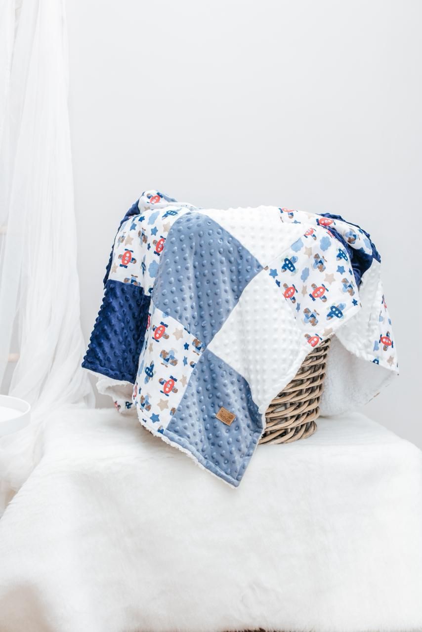A patchwork baby blanket with blue minky fabric and airplane print pattern draped over a wicker basket.