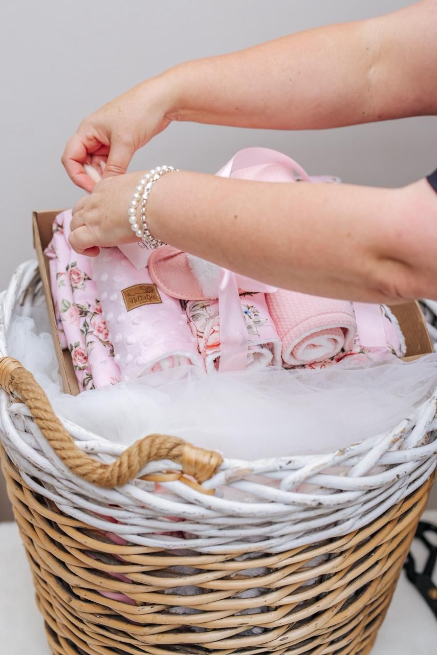 Hands arranging pink and white baby blankets in a woven basket display.