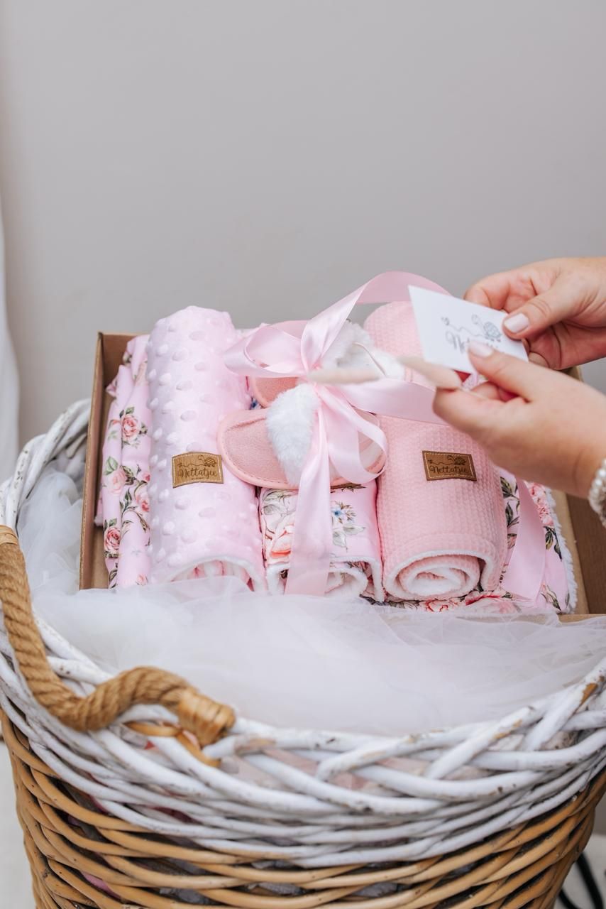 Small pink party favor boxes with bows being arranged in a white-lined wicker basket.