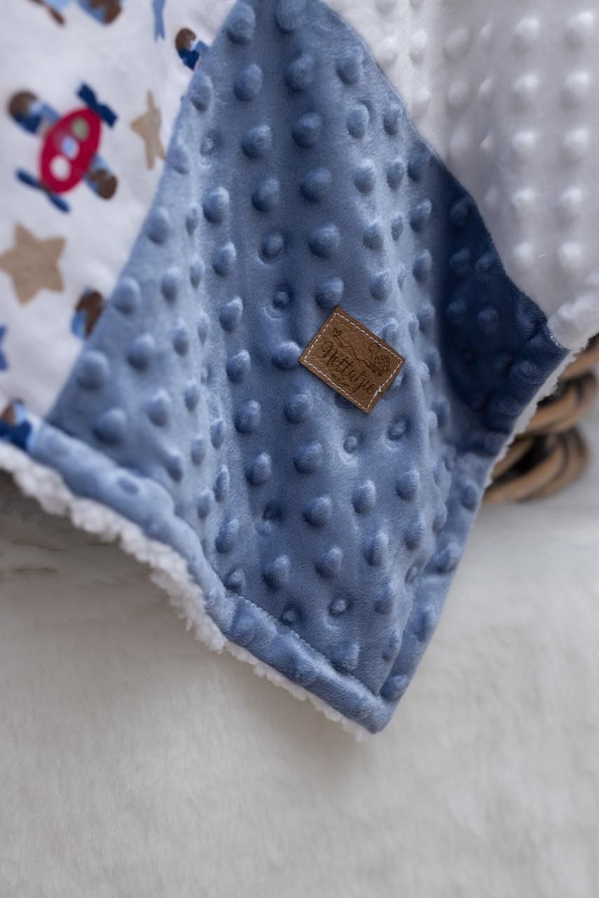 Close-up detail of a blue minky dot baby blanket with white trim and small decorative tags.