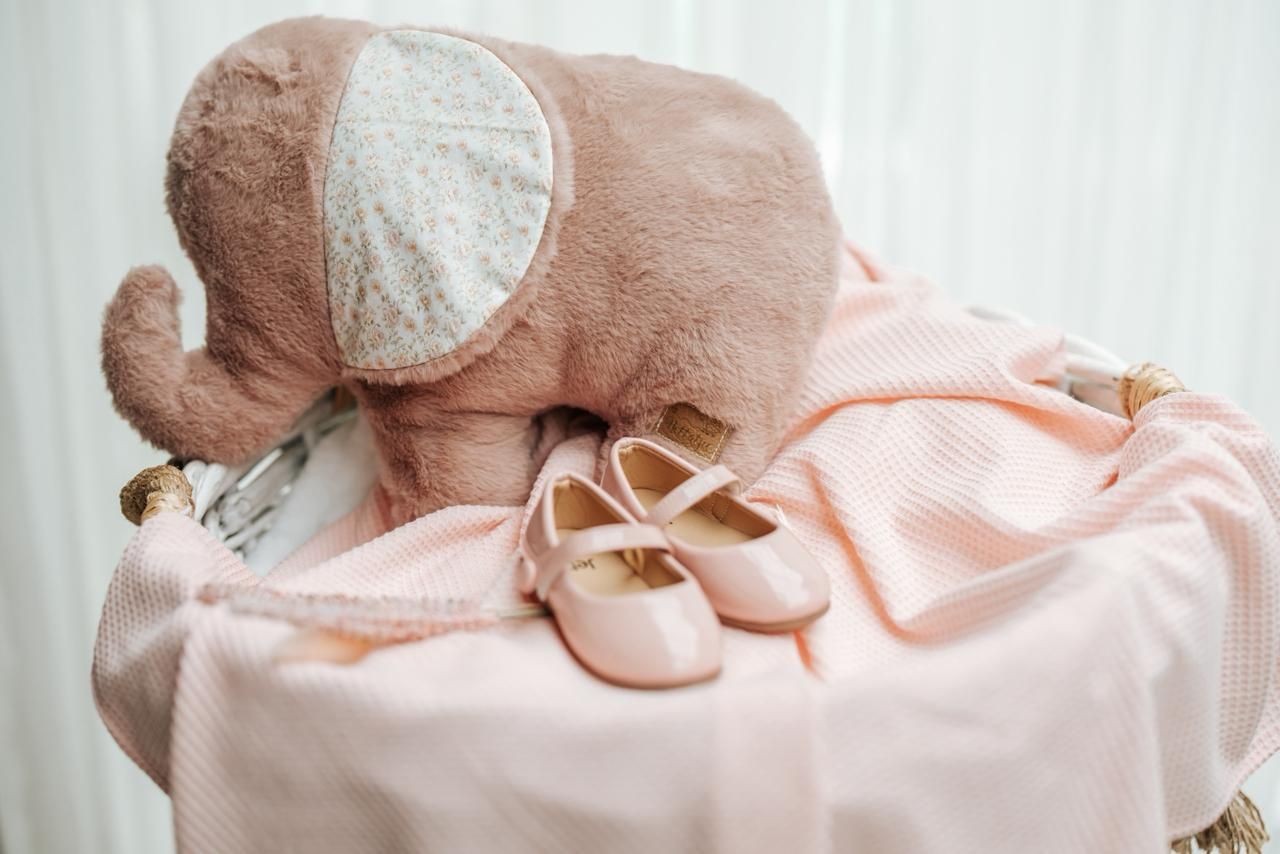 A sleeping baby in a pink onesie rests peacefully on a white surface.